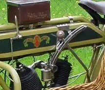 Links van de tank de schakelhefboom en het draaihendel voor de voorontsteking