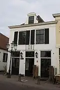 Huis met lijstgevel, gepleisterd, gewitte zijgevel. Achterhuis