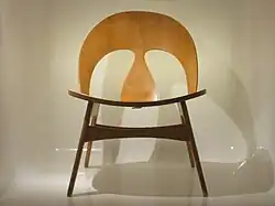 Foto van een stoel gemaakt van licht hout met een ronde rugleuning waarin twee uitsparingen zitten. De foto van de stoel is genomen tegen een witte achtergrond.