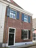 Huis met lijstgevel. Voorgevel grijs gepleisterd. Voordeur met bovenlicht