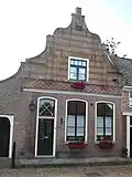 Huis met in- en uitgezwenkte gevel, versierd met pilasters en banden van gele baksteen. Gewijzigde pui