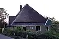 Forse stolphoeve, fraai gelegen in een bocht van de weg. Hoge, met geglazuurde pannen gedekte kap; boven de symmetrisch ingedeelde voorgevel een houten geveltop; boven de rechterzijgevel eveneens een houten top