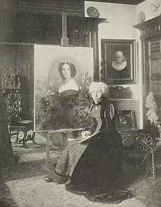 Mevr. Kate Bisschop-Swift in haar atelier bij het door haar geschilderde portret van koningin Sophie (1902)