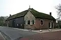 Boerderij, met woongedeelte evenwijdig aan de weg en loodrecht daarop gebouwde stal, waarvan de linker zijgevel ten dele uit gepotdekselde delen bestaat. De stal draagt een rieten wolfdak; over het woonhuis een rieten zadeldak. Links opkamer. Vensters met luiken en goede roedenverdeling