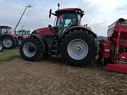 Zijaanzicht van een rode tractor met achterop een woeler en daarachter een zaaimachine