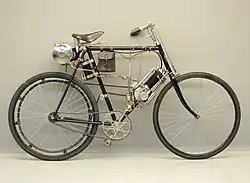 Clément 1¼ pk (125 cc) 1902 met bobine-ontsteking. De bobine zit onder het zadel, de loodaccu in het tasje aan de framebuis.
