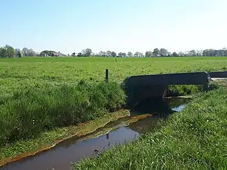 Het Dalemstroompje, met een bruggetje, die een verbinding vormt tussen beide weilanden, en op de achtergrond de Hapertse korenmolen.