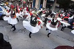 Momogeri (beschermers van Momos) stoppen bij huizen, winkels en kruispunten en dansen een expressieve traditionele dans met kleurrijke wandelstokken, linten en bellen, terwijl ze liedjes zingen over actuele onderwerpen.