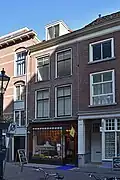 Winkelwoonhuis met voorgevel in sobere 19de-eeuwse vormen. Winkelpui in traditionalistische vormen uit ca. 1925.