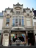 Winkel-woonhuis op rechthoekige plattegrond in overgangsarchitectuur met zowel historiserende als aan de Weense Sezession ontleende motieven. Het winkel-woonhuis is opgenomen in een gesloten gevelrij