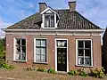 Dorpshuis met zesruitsvensters en versierde kroonlijst onder schilddak met hoekschoorsteen