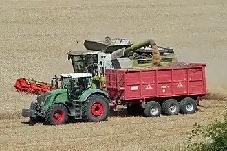 Kipper die naast lossende maaidorser rijdt