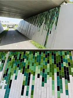 Op de betonnen randen van de fietstegel zijn tegeltableaus aangebracht. De kleuren van de tegels (groen, grauw en grijs) zijn geïnspireerd op de tinten die normaal ontstaan op beton door inwerking van de natuur. De tegels zijn gemaakt door Tichelaar, Makkum.