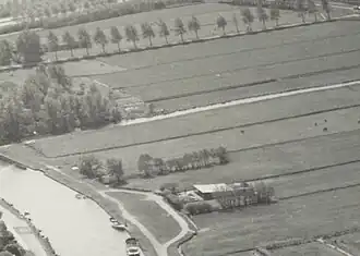Luchtfoto uit 1983 met in het midden tussen de Fuikvaart en een boerderij de voormalige begraafplaats gemarkeerd door een smal rijtje bomen