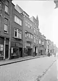 De straat omstreeks of iets na 1938. Van links naar rechts: inleggerij en azijnfabriek Roghmans, de rund-, kalfs- en varkensslagerijslagerij Rosendaal-Wouters, hoefsmid Uijen en de allereerste vestiging van Radio De Kroon
