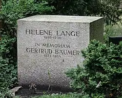 Foto van de grafsteen van Helene Lange. Het vierkante blok staat tussen groene planten en is aan de voorzijde wat vies door modder.