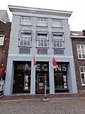 Huis met brede, gebosseerd witgepleisterde lijstgevel. Moderne etalages