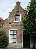 Huis. In- en uitgezwenkte topgevel met gemetselde pilasters. Pui gewijzigd