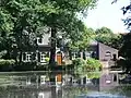 Voormalige slottermolen, resten van de voormalige watermolen en een woonhuis met wolfdak, rondboogvensters en een ingang in een rondbogige hardstenen omraming. Molenvijver