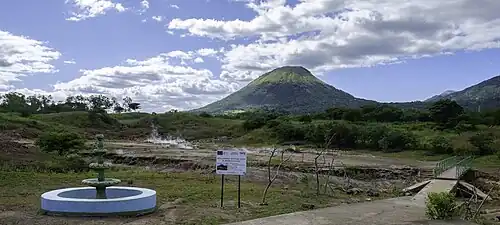 Overzicht met de vulkaan op de achtergrond. Rechtsachter een nieuwe brug voor wanneer het water in het riviertje langs de bronnen hoger staat.