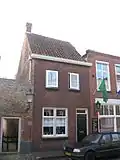 Achter een moderne gevel een huis met dwars zadeldak tussen zijtopgevels