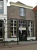 Huis met lijstgevel met ingezwenkte zijkanten en met schuiframen en winkel-ingangspartij uit de bouwtijd