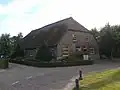 Boerderij van het in de Langstraat gebruikelijke type. Met riet gedekt wolfdak, voorgevel met vlechtingen, vensters met zes-, negen-, twaalf- en twintigruitsschuiframen