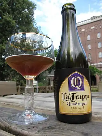 Een geopende fles La Trappe Quadrupel Oak Aged, uitgeschonken in het bijbehorende La Trappe glas.