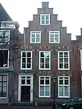 Pand met trapgevel met geblokte togen boven de vensters. Hardstenen stoep met palen. Houten deuromlijsting, voordeur en beneden vensters gewijzigd