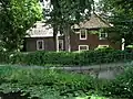 Op de hoek van de Kluiskade een boerderij op L-vormige plattegrond, schilderachtig gelegen, met pannen schilddak en voorgevel met ingezwenkte zijkanten. Oude kozijnen