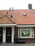 Blok met 8 woningen, gecombineerde toegangen van twee woningen onder een ingestoken schilddak, zijkant met houten topgevel, aan zuidkant toegangspoort tot binnenterrein, onderdeel van complex bejaardenwoningen in Tuindorp Nieuwendam