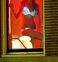 Prostituee achter een rood verlicht raam gekleed met door blacklight geaccentueerde lingerie