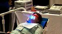 Foto van een vrouw in een tandartsstoel die haar tanden gebleekt krijgt