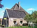 Stolphoeve met kort uitgebouwd vooreind. Links achter aangebouwd een schuurtje onder zadeldak; aan de achterzijde een nieuwe schuur