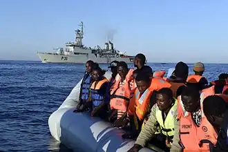 Een rubberboot met Afrikaanse migranten, met op de achtergrond het Ierse patrouilleschip LÉ Eithne.