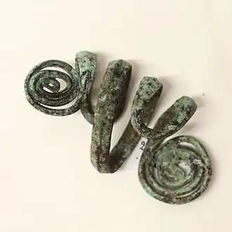 hanger in de vorm van een ramskop.Bronzen sieraad uit graf nr. 9. te Koban, 9e eeuw v.Chr.