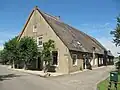 Boerderij onder hoog, rieten zadeldak, dat zowel het woonhuis als het daarachter gelegen bedrijfsgedeelte overdekt. In de puntgevel aan de voorzijde en in de zijgevel ten dele nog vensters met ramen in kleine roedenverdeling. Boven de rechter zijgevel een dakkapel en in de zijgevel van de stal inrijdeuren onder opgewipt dakgedeelte