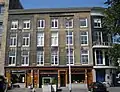 Pand met afgeronde hoek, drie verdiepingen en hoofdgestel met in het fries panelen, waarboven rijk geprofileerde kroonlijst. In 1910 van een nieuwe natuurstenen gevel voorzien