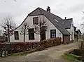 Boerderij onder rieten wolfdak met rechts een uitgebouwde zijkamer met puntgevel. In de gepleisterde voorgevel vensters met luiken en zesruitsschuiframen