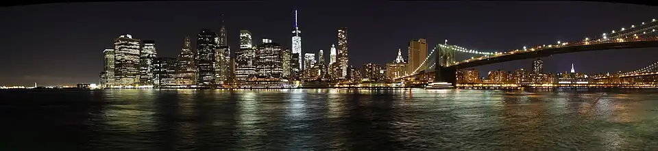 De skyline van Lower Manhattan in het echt, gezien aan de overkant van de East River vanaf Brooklyn anno 2013. Te zien zijn de Freedom Tower, Brooklyn Bridge, Pier 17, en andere oriëntatiepunten die een prominente plek in Dammers' schilderij hebben.