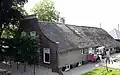 Goed bewaarde boerderij met ingezwenkte gevel, bekroond door een lijst. Op het hoge rieten dak een schoorsteen met smeedijzeren bekroning