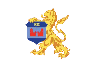 alt=Schild: Azuur met lichtblauwe band, "1933" in goud, en een rood kasteel.
Schildhouder: Gouden leeuw