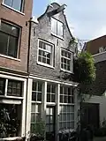Huis met latere gevel, voorzien van een vroeg-19e-eeuwse houten pui met goede roedenverdeling en beglaasde empire deur en bekroond door een klokvormige top onder rollagen