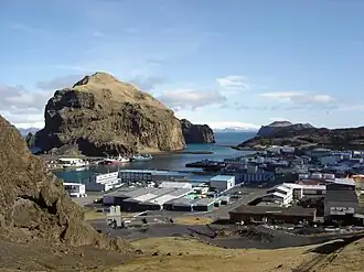 Het stadje Vestmannaeyjar op het grootste eiland Heimaey, gezien vanaf de hellingen van de berg Háhá. De berg links heet Heimaklettur. Achter het lavaveld rechts is Bjarnaey te zien.