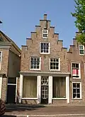Pand onder zadeldak tegen gerestaureerde trapgevel met toppilaster